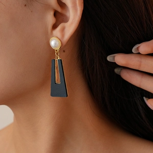 Détail de boucles d'oreilles noires géométriques avec pendentif trapèze et perle