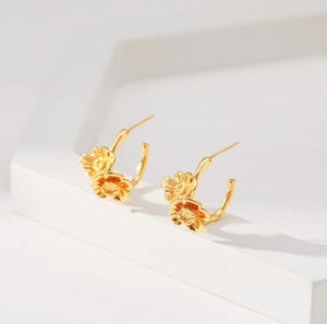 Elegant 18K gold plated brass flower stud earrings on a geometric white tray pedestal
