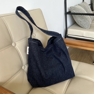 Borsa tote in denim blu scuro con cuciture a contrasto su una sedia in pelle beige