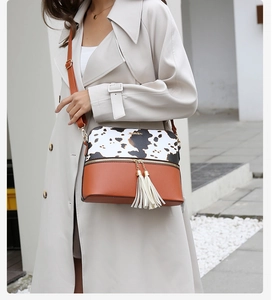 Detail of cow print and brown leather shoulder bag with tassels and gold logo
