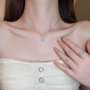 Close-up of a model wearing a silver necklace and ring set with square light blue gemstones