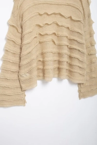 Detail of loose beige knit sweater with layered ruffle textures and soft wool fabric