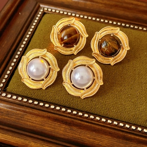 Macro detail of vintage gold pearl and tiger eye stone earrings in a green velvet box