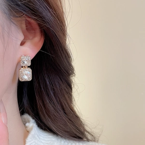 Detail of square gold earrings with clear crystals shown on ear for size and sparkle