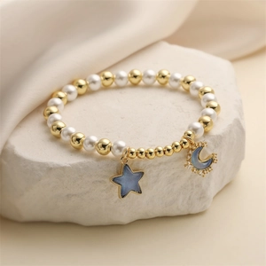 Detailed close-up of blue star and moon pendants on a beaded pearl and gold bracelet