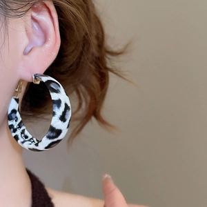 Close-up of model wearing large black and white leopard print resin hoop earrings with gold pins