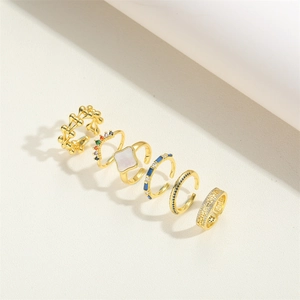 Detail view of 6 gold stacking rings with blue stones and square shell inlay on white surface