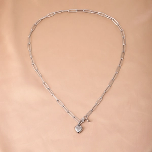 Macro shot of silver heart pendant and textured paperclip chain on soft satin background