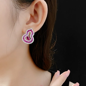 Close-up of elegant hollow gourd earrings with pink zircon on model with dark backdrop