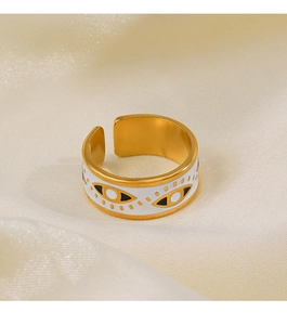 Détail de bague œil maléfique dorée en émail blanc sur fond de tissu en soie beige