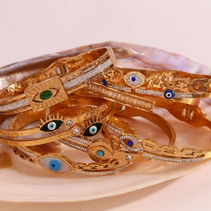 Close-up of stacked 18K gold-plated Evil Eye bracelets on natural shell background