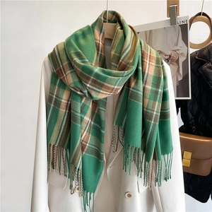 Dettaglio di sciarpa a quadri verde e marrone con nappe su un blazer bianco