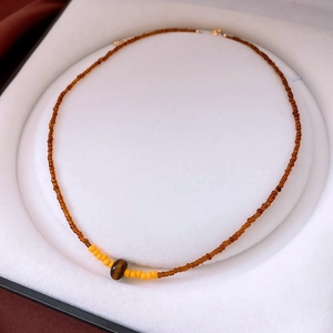 Détail du collier de perles en œil de tigre et perles d'ambre dans un écrin à bijoux blanc