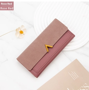 Detail of rose red long wallet with gold V-buckle and textured matte finish over marble