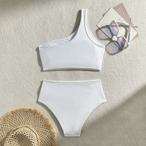 Detailed flat lay of white one-shoulder bikini with high-waisted bottom and vacation props