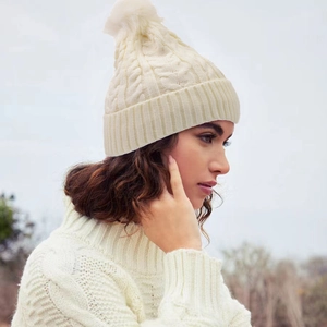Détail d'un bonnet en maille torsadée blanc cassé avec pompon et revers côtelé