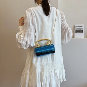 Electric blue cylindrical evening bag with gold lion handle on a white dress background