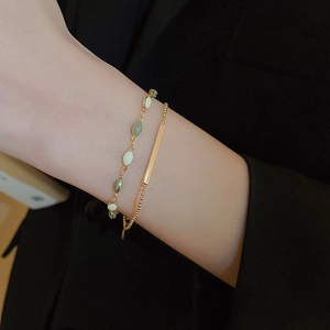 Close-up of gold double-layer chain bracelet with green and white oval bead charms