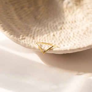 Detailed view of a gold V-shaped ring with a small birthstone on a textured background