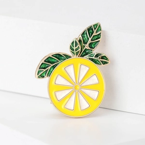 Macro shot of yellow enamel lemon slice brooch with green leaf and golden metal frame