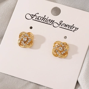 Macro view of gold flower earrings with crystals on white jewelry card and silk