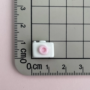 Detailed top view of a miniature 1.5cm white and pink resin camera accessory on a scale ruler