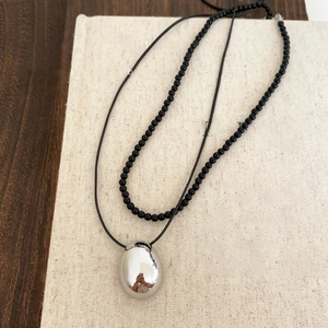 Detail view of oval silver pendant on black leather cord and beaded necklace design