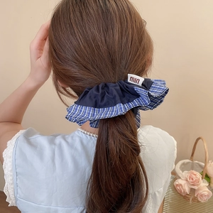 Détail d'un chouchou en tissu quadrillé bleu avec étiquette m sur une queue de cheval