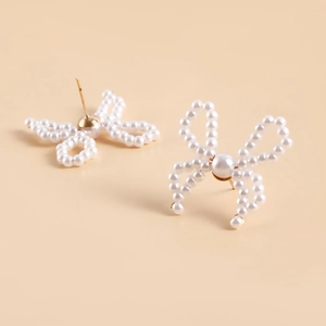 Detail of handmade pearl bow earrings with gold-tone metal base on beige background