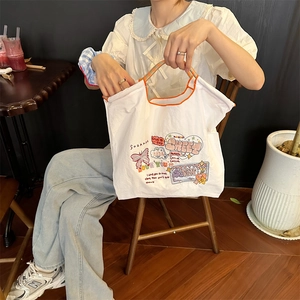 Detail der weißen Canvas-Tasche mit bunten Stickereien und orangefarbenen Tragegriffen