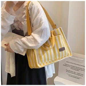 Close-up of yellow striped canvas tote bag with leather tag worn by a model