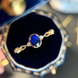 Detailed close-up of a gold oval blue sapphire ring in a vintage blue velvet jewelry box