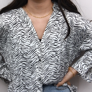 Close-up of golden paperclip chain necklace and bracelet on model wearing zebra shirt
