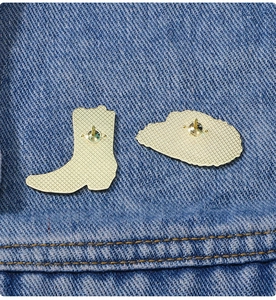 Detail showing gold metal back of boot brooch with anti-slip texture on denim fabric