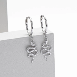 Macro detail showing textured silver snake earrings on a minimalist grey pedestal