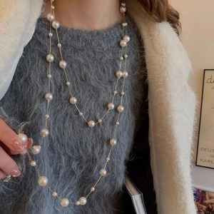 Détail d'un collier de perles multicouche avec chaîne dorée sur pull en maille grise
