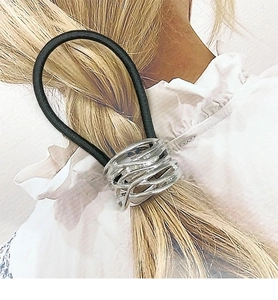 Detail of silver irregular metal accessory on black elastic hair tie on blonde hair