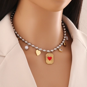Detail of silver bead necklace with gold rectangle charm and red heart on model