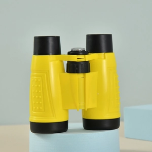Yellow toy binoculars for kids on blue stand featuring black eyepieces and focusing wheel