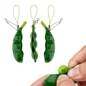 Detail showing hand squeezing green pea pod keychain with cartoon face popping out