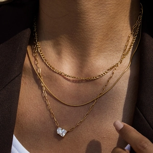 Close-up of gold layered necklace set featuring heart-cut crystal pendant on paperclip chain