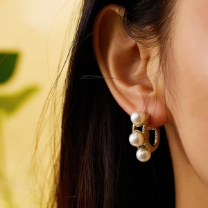 Close-up of three white pearls on a gold hoop earring worn on an earlobe