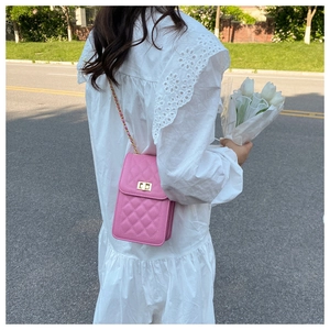 Pink quilted crossbody phone bag with gold chain strap shown on model in sunny outdoor setting