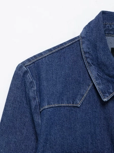 Vue détaillée des surpiqûres orange contrastées sur un ensemble en jean bleu foncé