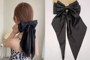 Detail showing the large black satin bow hair clip with long ribbons on a model and tray