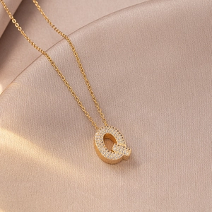 Macro shot of gold-plated letter Q pendant with cubic zirconia on champagne satin fabric