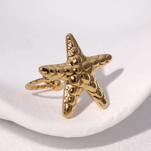 Minimalist golden starfish ring with textured relief pattern on a white stone tray