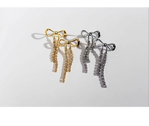 Detalle de los pendientes de lazo con diamantes de imitación y borlas en oro y plata