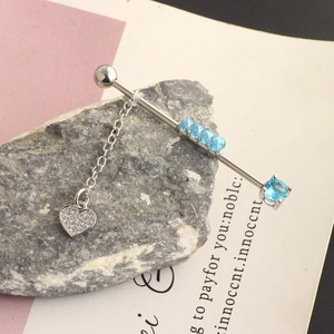 Detail of stainless steel industrial barbell with blue gem, chain, and heart pendant