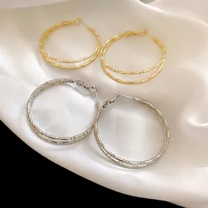 Bamboo-textured double layer hoop earrings in gold and silver finish on white silk background